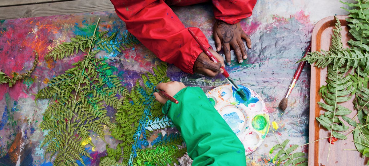 Två barnhänder som målar på ormbunksblad.