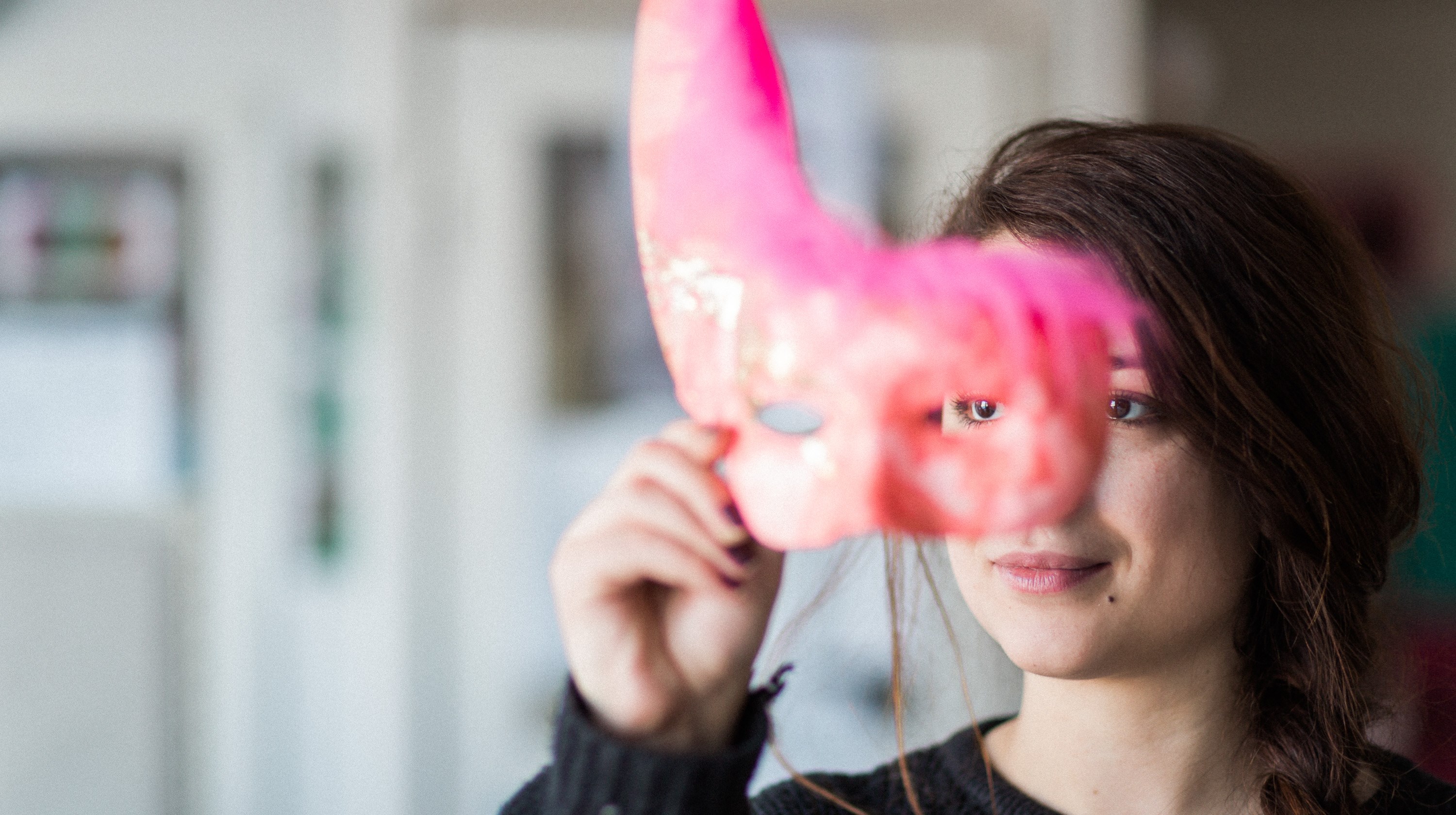 En ung kvinna som håller upp en rosa mask framför sitt ansikte